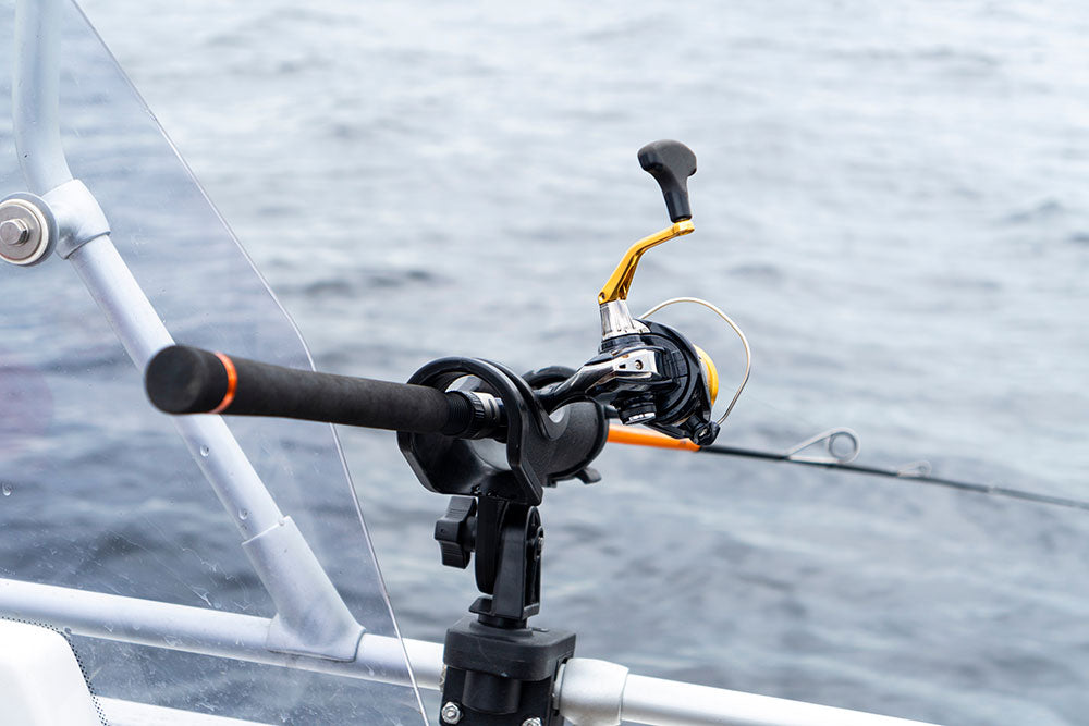 View of a mounted fishing reel and holder on a boat with a scenic sea backdrop.